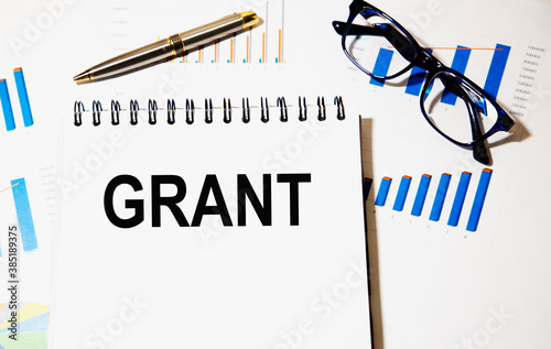 Grant text on a notepad, next to it are glasses, pen, graphics.