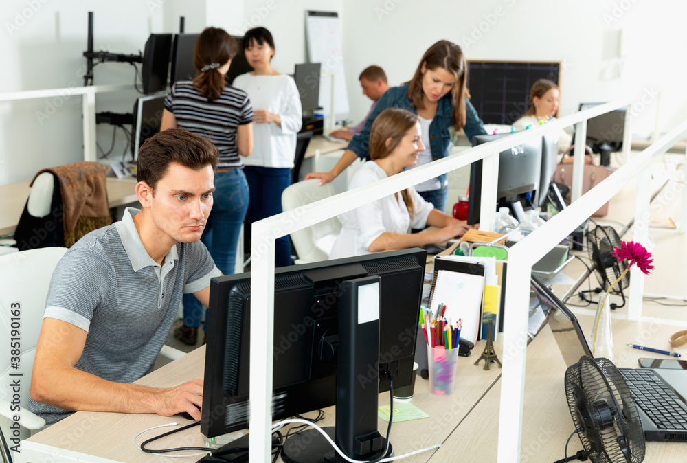 Fototapeta premium Handsome young diligent cheerful man confidently working on computer in modern open plan office