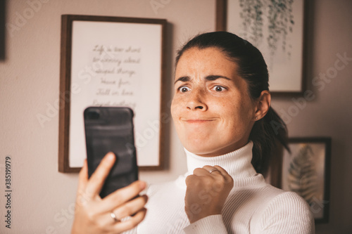 Angry agitated young woman, angry and holding the phone waiting for a call, looking at the smartphone, depressed sad jealous girl after a fight writes to the guy on the mobile phone.