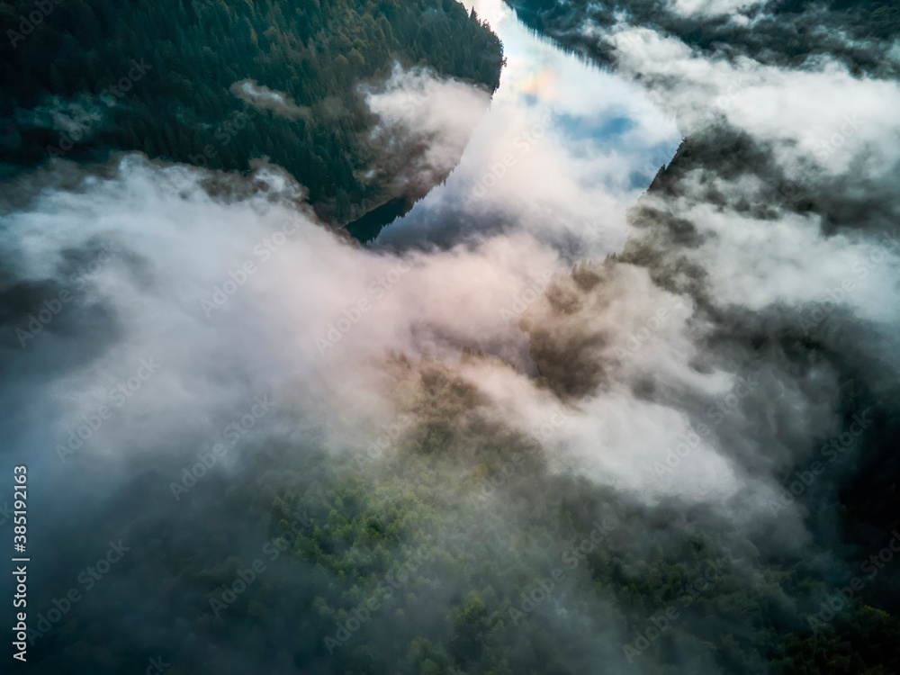 Aerial view clouds over the forest and lake at sunrise. View from drone. Aerial top view cloudscape. Transylvania, Romania
