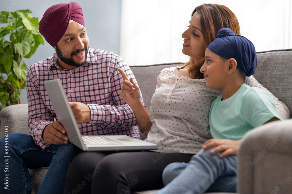 A SIKH PARENTS LOOKING AT EACH OTHER WHILE TEACHING SON WITH LAPTOP A SIKH PARENTS LOOKING AT EACH OTHER WHILE TEACHING SON WITH LAPTOP