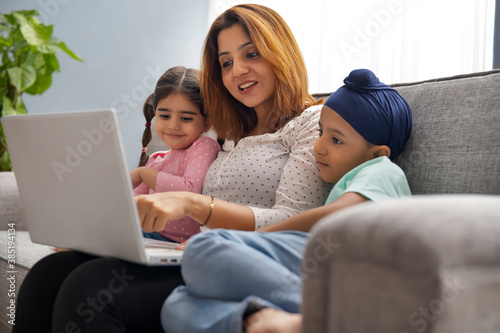 A SIKH MOTHER CHEERFULLY TEACHING HER SON AND DAUGHTER ON A LAPTOP AND KIDS LARNING CAREFULLY photo