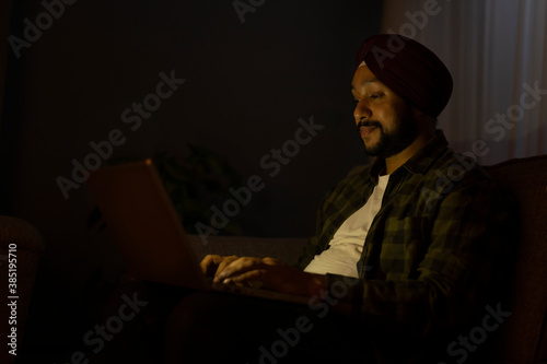 A SIKH MAN SITTING AND WORKING ON LAPTOP DURING NIGHT	