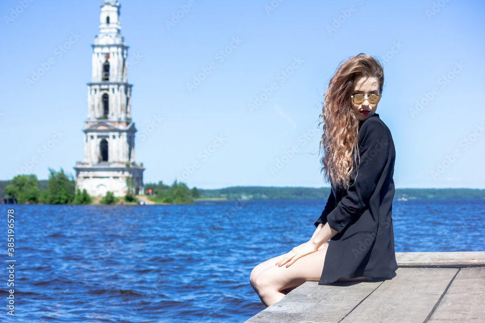 A girl in a black jacket against the background of the Uglich reservoir Kalyazin city. Rocky shore.