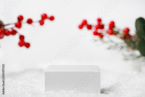 Winter Christmas scene with Ilex twigs on the background. Light white geometric pedestal for product presentation, cosmetics. Snow cube stand for advertising display