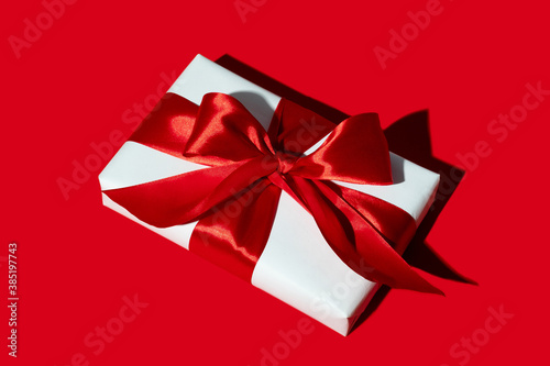 Holiday surprise. Long-distance gift. Care package. Special day congratulation. Present wrapped in white box with ribbon bow isolated on red background.