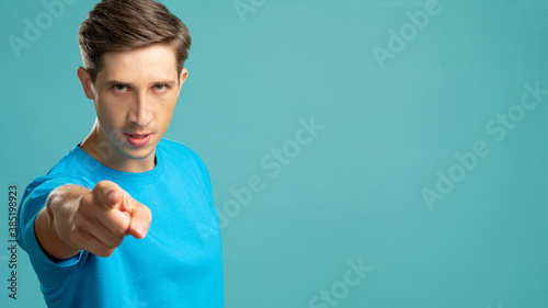 Angry man. Threaten gesture. Critical abusing. Aggressive emotion. Young blaming guy looking at camera pointing finger isolated on blue copy space. photo