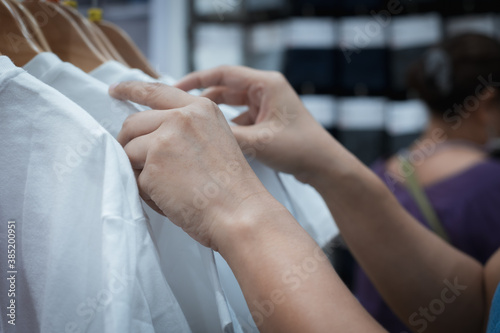 Close up on woman hand choosing discount t-shirt clothes in shopping mall, searching or buying cheap cotton shirt on rack hanger.