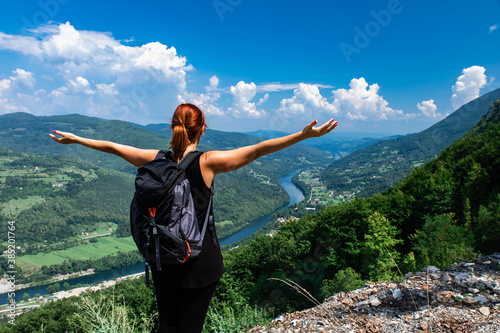 Rear view of female hiker with backpack standing on top of the mountain with her arms outstretched enjoying the view during the day.