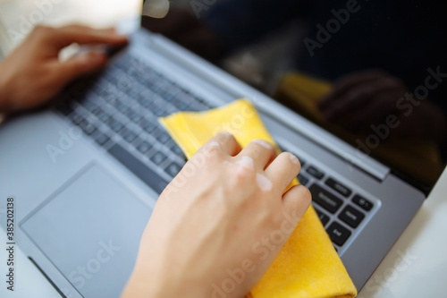 Closeup of the man's hands cleaning laptop's keyboard with a yellow rag and sanitizer to prevent coronavirus spread during global pandemic quarantine. Health care and removing bacteria from gadgets.