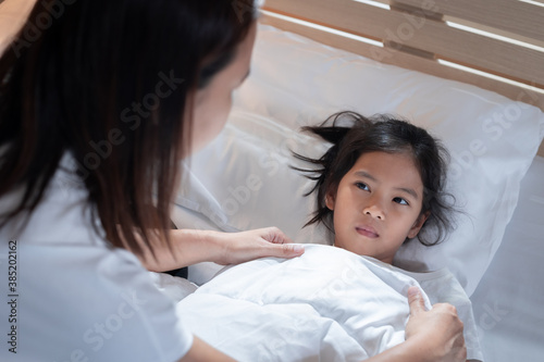 Sick asian child girl get sick and sleep on the bed, mother taking care and cover the blanket on her daughter at home.