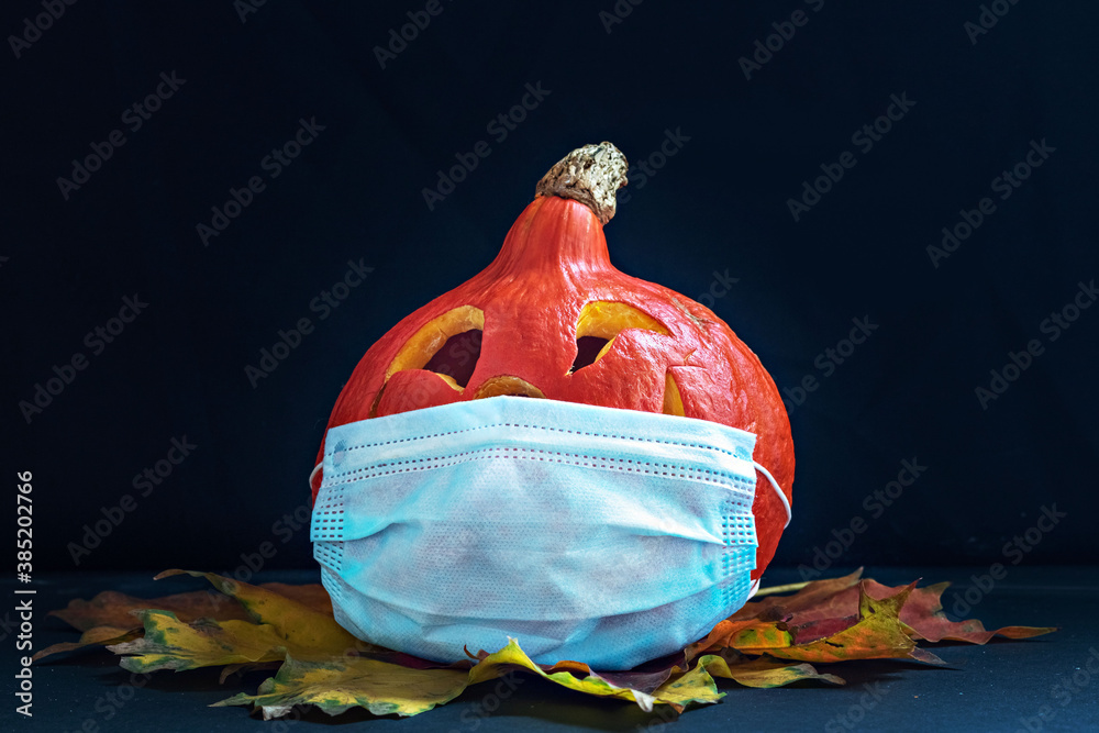 Pumpkin in a medical mask with autumn leaves on a dark background. Jack's Lantern. Halloween Decorations 2020. Coronavirus pandemic
