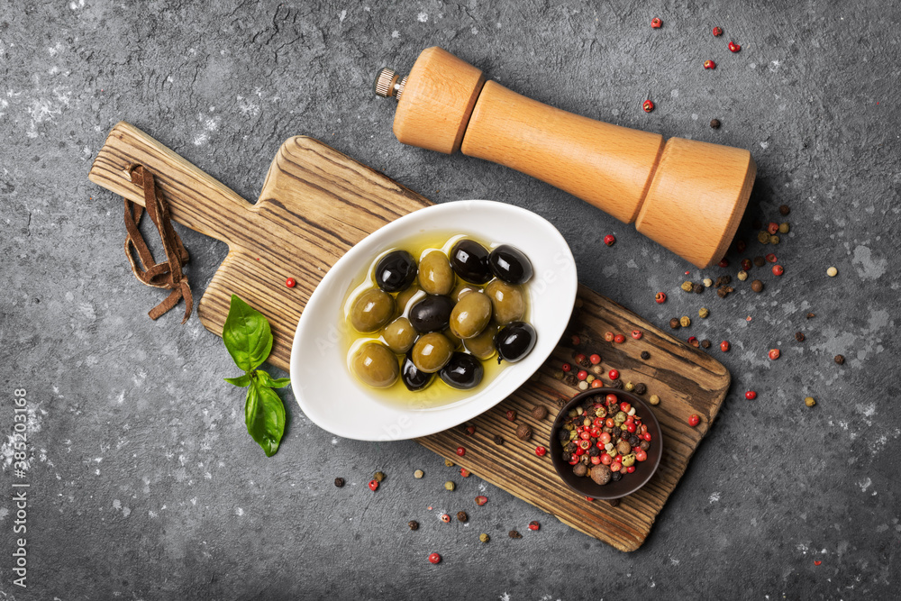 Bowl of delicious green and black olives in oil with pepper mill