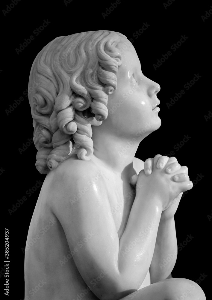 Boy statue pray to God with hands held together. Beautiful old stone statue of praying child isolated on black background