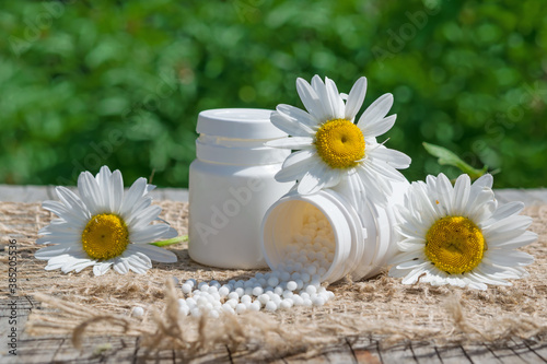 The concept of homeopathy. Homeopathic balls, pills from a plastic jar, flowers of the medicinal plant chamomile , green background. Alternative, medicine,copy space