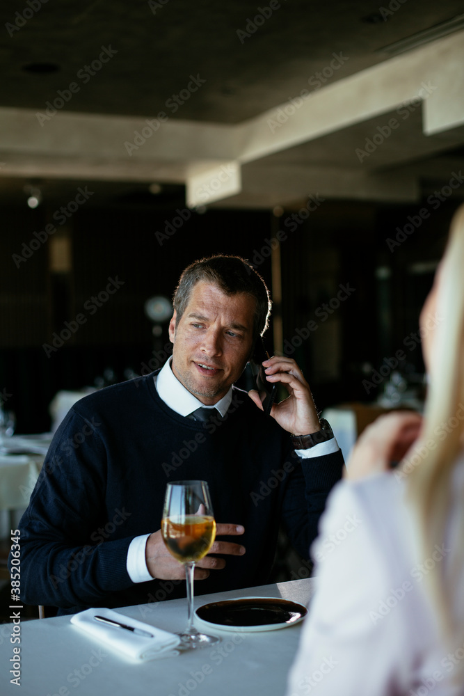 Handsome businessman dressed in the suit drinking wine. Businessman talking to the phone...