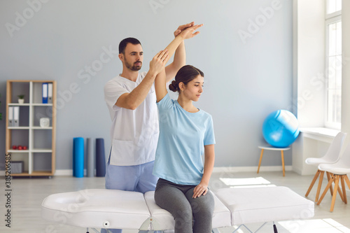 Licensed chiropractor or physiotherapist helping young female patient in modern clinic