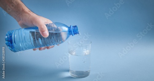 Male hand holding water bottle pouring water into glass.