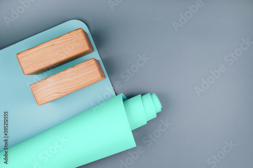 Top view of blue green yoga mat and two wooden blocks on pastel grey background. Yoga pilates Sport concept. Flat Lay. Copy space.