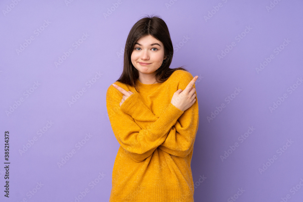 Naklejka premium Young Ukrainian teenager girl over isolated purple background pointing to the laterals having doubts