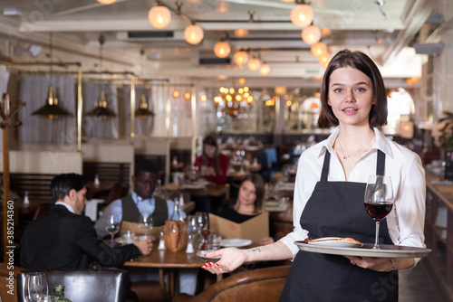 Portrait of smiling waitress with serving tray meeting restaurant guests. © JackF
