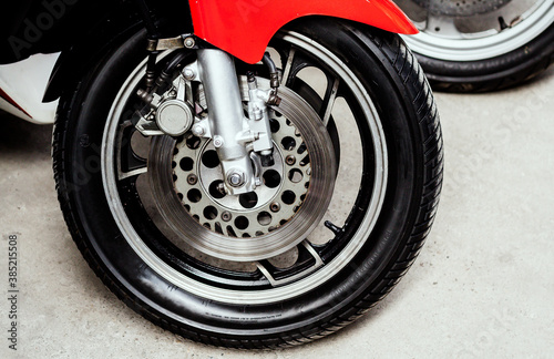 Front wheel with brake discs, caliper of sports motorcycle close-up on concrete. Rubber with chrome alloy disc, brake system of road bike in garage on repair. Moto tire and fork. Side view.