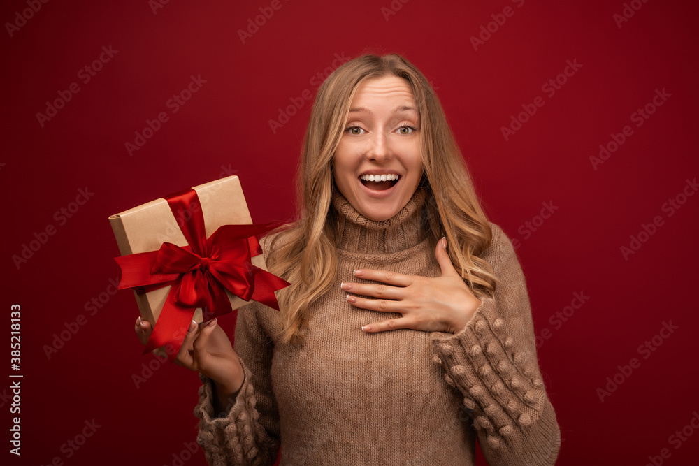 Charming blonde woman holding gift with red ribbon. Studio shot red background. New Year Birthday Holiday concept Charming blonde woman holding gift with red ribbon. Studio shot red background. New Year Birthday Holiday concept