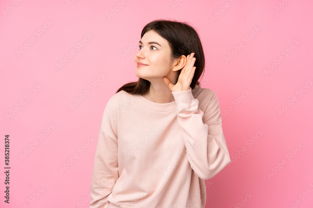 Young Ukrainian teenager girl over isolated pink background listening to something by putting hand on the ear Young Ukrainian teenager girl over isolated pink background listening to something by putting hand on the ear