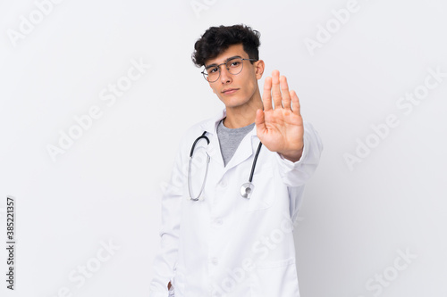Young Argentinian man over isolated white background wearing a doctor gown and making stop sign