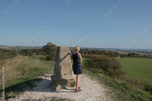 Adult Caucasian Female Leaning Against the Trig Point on the Top of Devil's Dyke Hill with the City of Brighton in the Distance on the South Downs in Rural West Sussex, England, UK photo