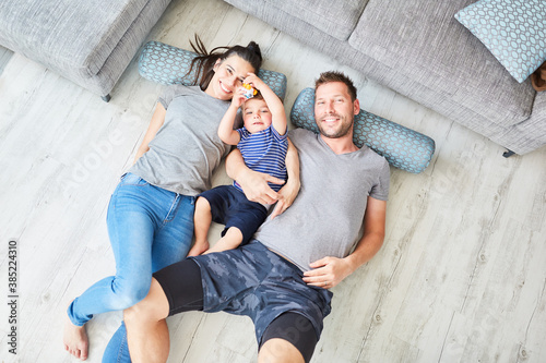 Parents and child are lying on the floor in the living room