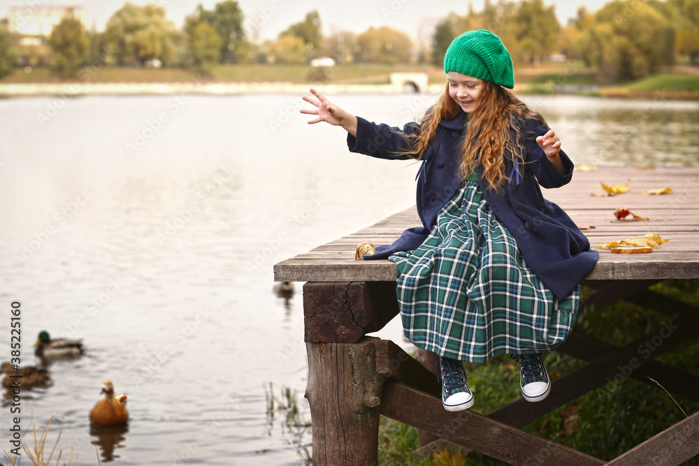 Naklejka premium Irish little red haired girl outdoor photo on fall lake landscape background feeding ducks