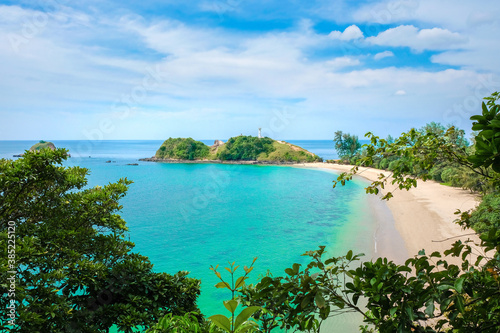 Beautiful exotic seascape. Deserted beach with yellow clean sand, turquoise sea, blue sky with clouds. There is a white lighthouse on the hill. Koh Lanta, Thailand