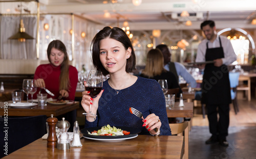 Attractive young woman enjoying dinner with glass of red wine alone in cozy restaurant