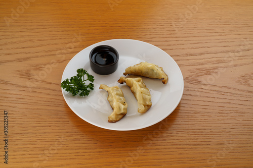 Gyozas on a white plate atop a wood table, 45 degree