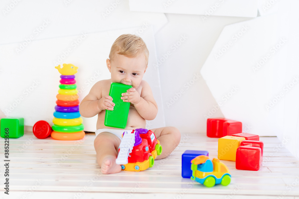 a small child a boy of six months plays with bright toys in a bright white room in diapers and nibbles them a small child a boy of six months plays with bright toys in a bright white room in diapers and nibbles them
