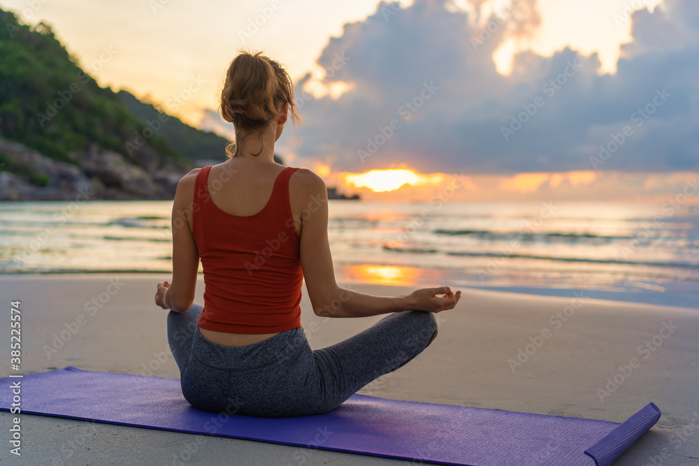 Yoga meditation. Woman sitting in lotus position and meditating at sunrise on the beach