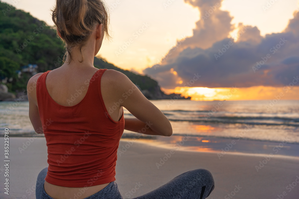 Woman practices yoga. Woman sitting in lotus position and meditating at sunrise on the beach
