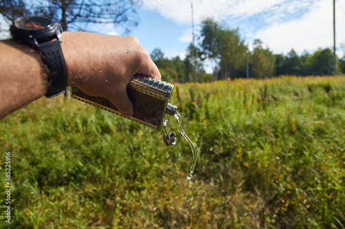A human hand holds a metal flask from which water flows.