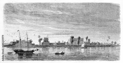 Horizontal view of Richard Toll fort, Senegal, far on a shore reflecting in calm water sailed by ships. Ancient grey tone etching style art by De B�rard, published on Le Tour du Monde, Paris, 1861 photo