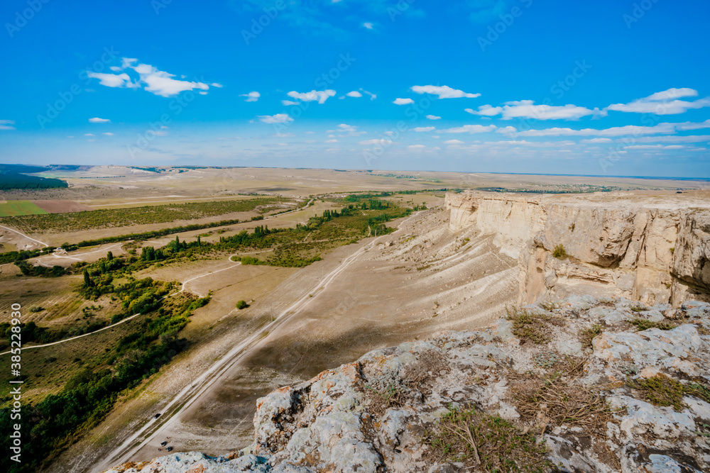 View from the height of the white rock and green valley. Blue sky, a small village at the bottom. Crimea View from the height of the white rock and green valley. Blue sky, a small village at the bottom. Crimea