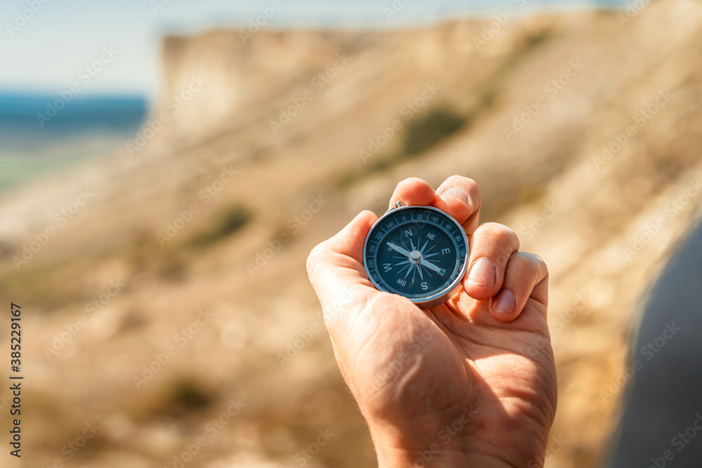 A male hiker is looking for a direction with a magnetic compass in the mountains in the fall. Man's hand holds a compass