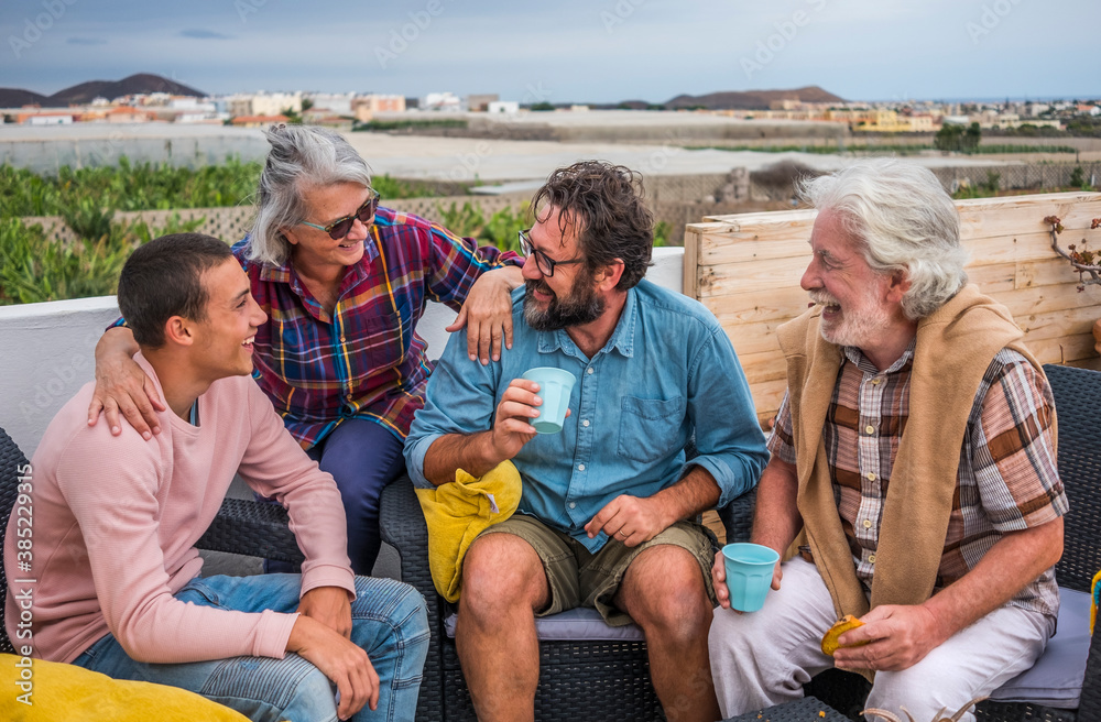 Group of smiling family sitting outdoor on the terrace with food and drink having fun together. Senior couple with mature son and teenage grandson