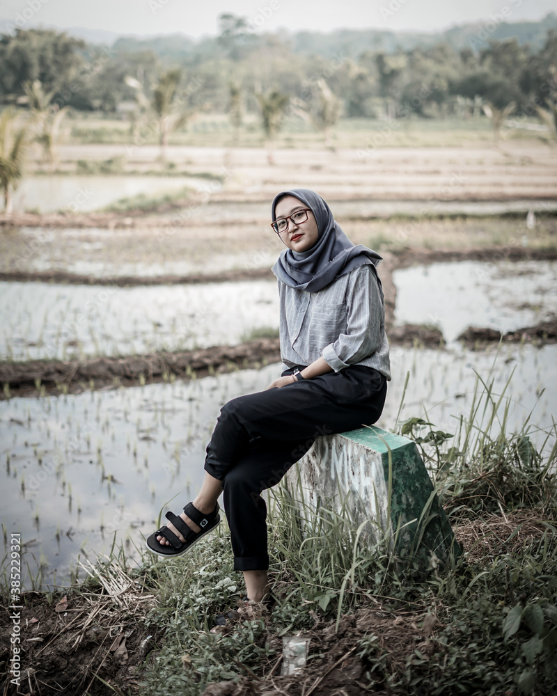Beautiful Asian Muslim woman posing and stylish with rice fields and trees as background. Beautiful Asian Muslim woman posing and stylish with rice fields and trees as background.
