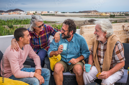 Group of smiling family sitting outdoor on the terrace with food and drink having fun together. Senior couple with mature son and teenage grandson