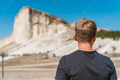 Rear view of a young man standing and looking out over a huge white rock, concept of travel and freedom, Crimea 