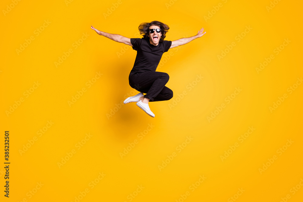 Full length body size portrait of man jumping high wearing black casual outfit sunglass shouting isolated on bright yellow color background