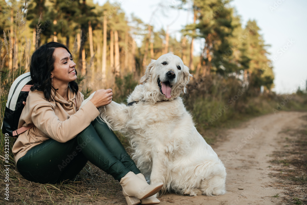 Εκτύπωση καμβά Brunette girl and white golden retriever dog on the forest path