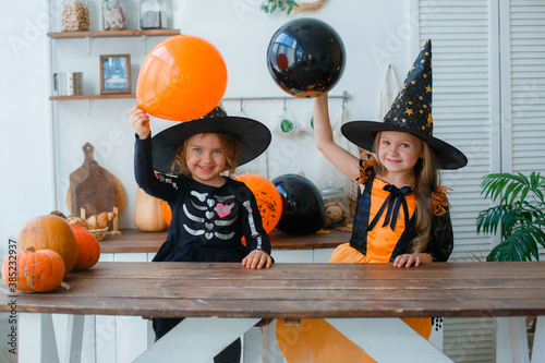 two little girls in witch costumes in the kitchen are playing with balloons for the Halloween holiday