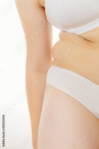 A woman in white underwear leans over and shows her fat crease on the side of her stomach on a white background